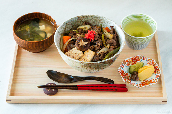 sukiyaki don on a wood tray next to soup and pickles