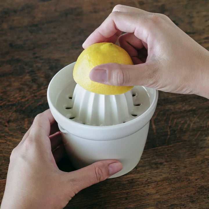 White ceramic citrus juicer in use, with a hand pressing a lemon over the ridged reamer, set on a wooden table.