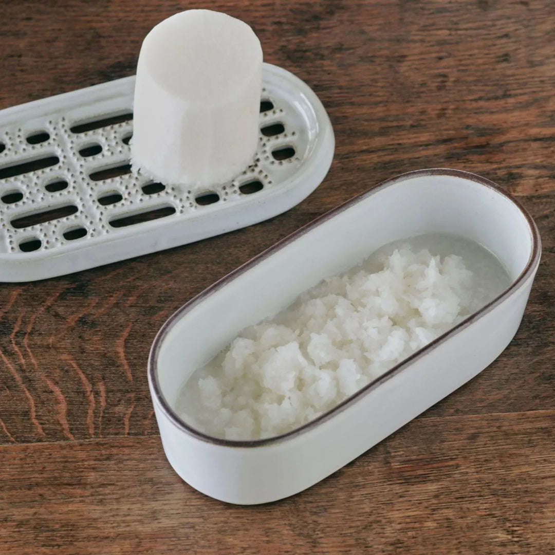 White ceramic daikon grater with grated radish collected in the matching serving dish, placed on a wooden table.
