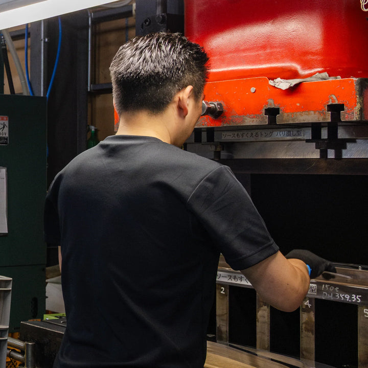Artisan operating a metal press in a factory workshop during the careful shaping of cookware parts