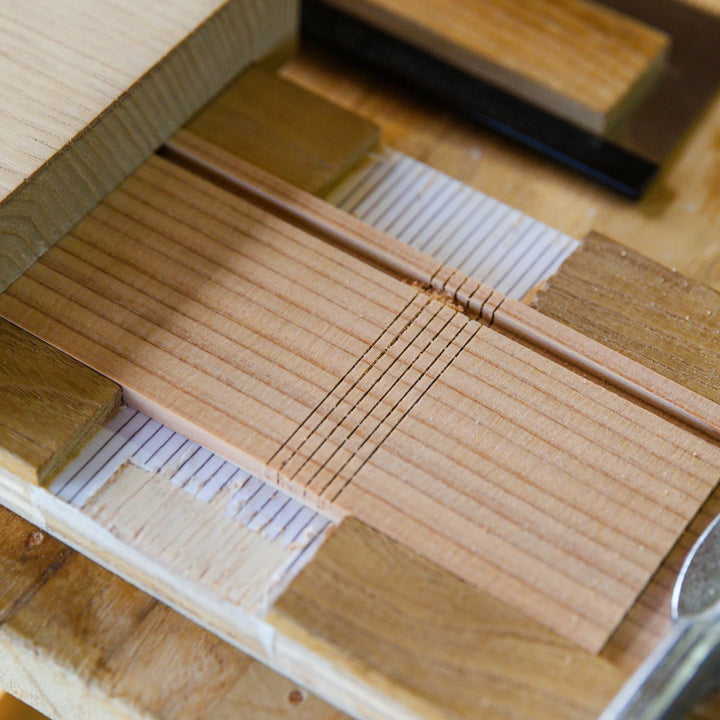 Close-up of precise grooves being carved into a thin wooden board, showing detailed craftsmanship and careful woodworking work
