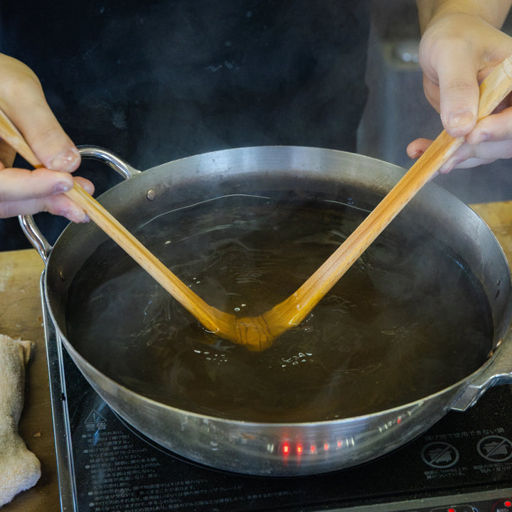 Steam rises as artisan shapes wooden utensils in hot water during handcrafted production