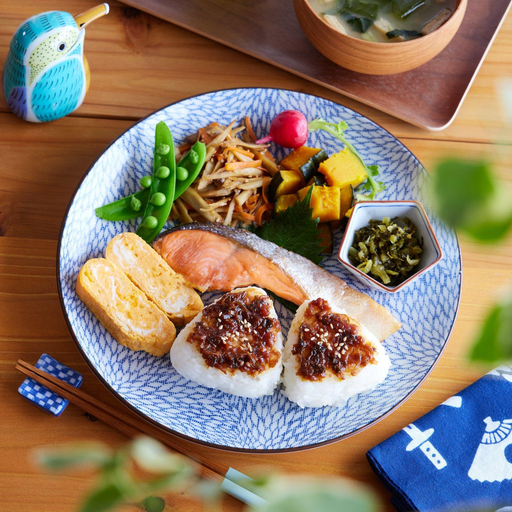 Traditional Japanese breakfast on a Blue Willow dinner plate with salmon, tamagoyaki, rice balls, and sides.