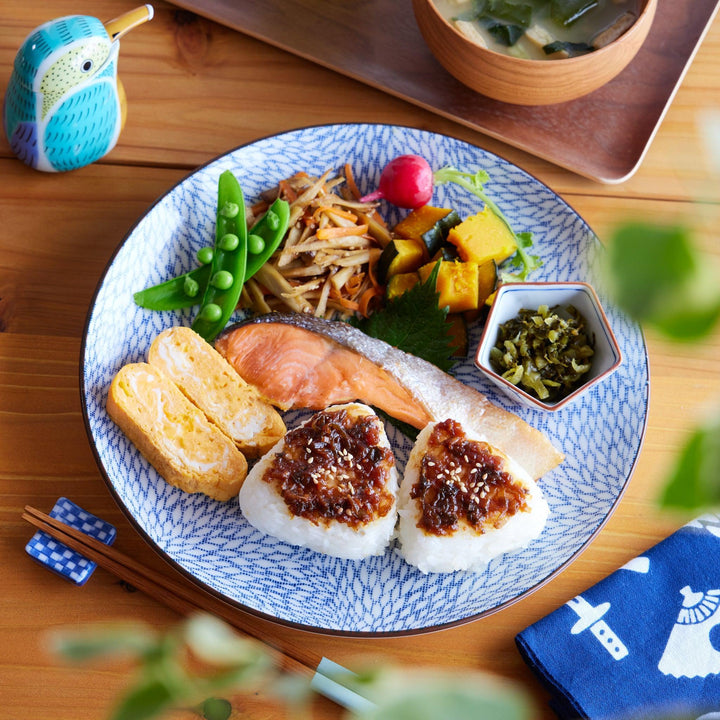 Traditional Japanese breakfast on a Blue Willow dinner plate with salmon, tamagoyaki, rice balls, and sides.