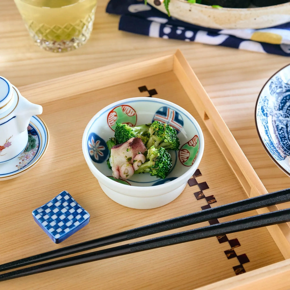 A small colorful soy sauce dish with broccoli and octopus Japanese salad placed on a light wooden tray.