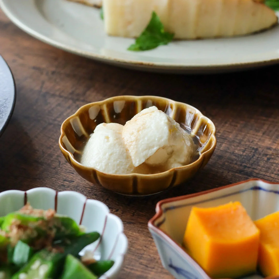 A small ceramic Japanese condiment bowl with scalloped flower-petal edges, filled with tofu in a Japanese meal.