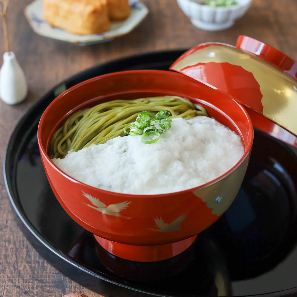 A red lacquer miso soup bowl with gold flying crane design, filled with tororo and green tea soba noodles.