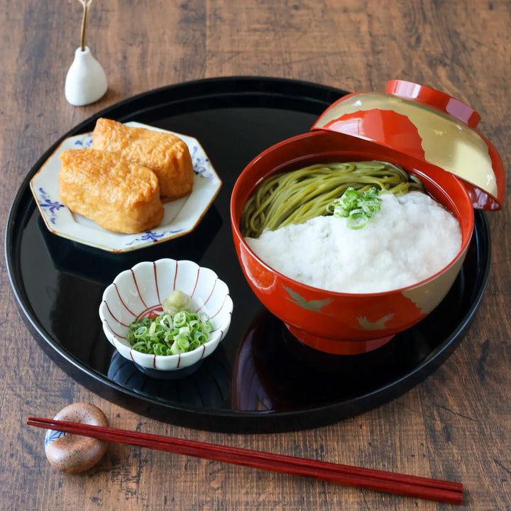 Japanese meal with green tea soba in a red crane miso soup bowl, served with inari sushi and condiments on a black tray.