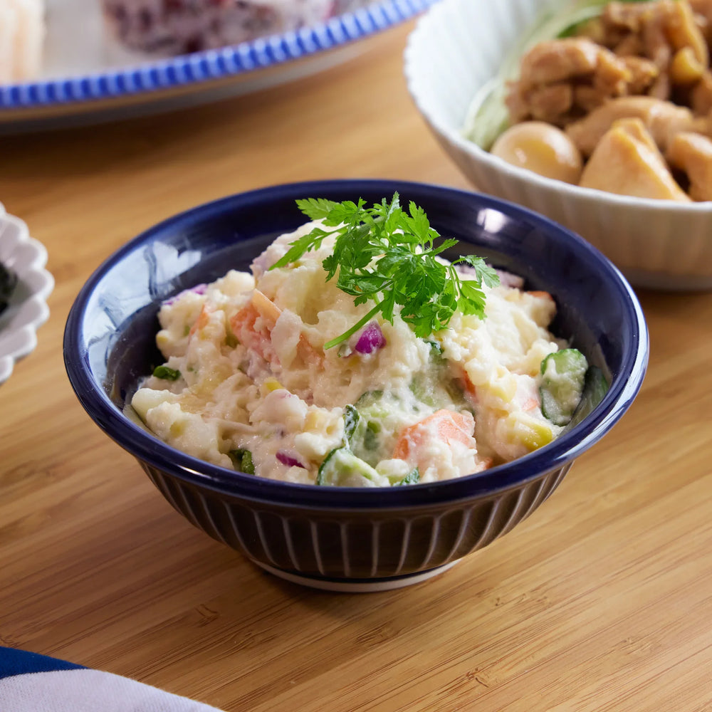 Japanese potato salad served in a deep blue Ginpo Kikka Lapis ceramic bowl, garnished with fresh herbs.