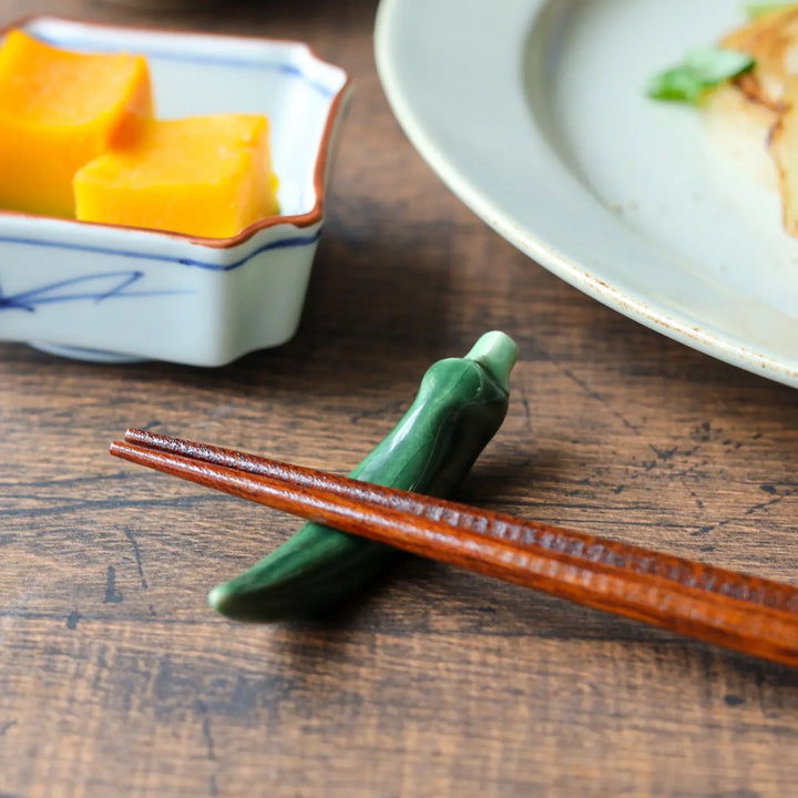 A ceramic Japanese chopstick rest shaped like a green chili pepper, holding wooden chopsticks.