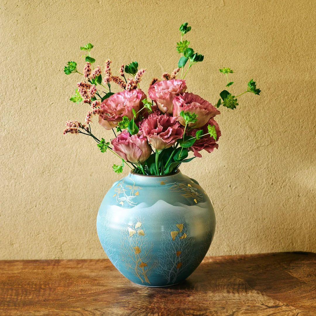 Hand-painted turquoise round vase with gold leaf motifs showcasing a lush bouquet of ruffled pink blooms and green foliage.