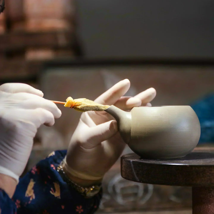 Artisan refining the spout of a clay teapot with careful hand finishing in a traditional pottery workshop