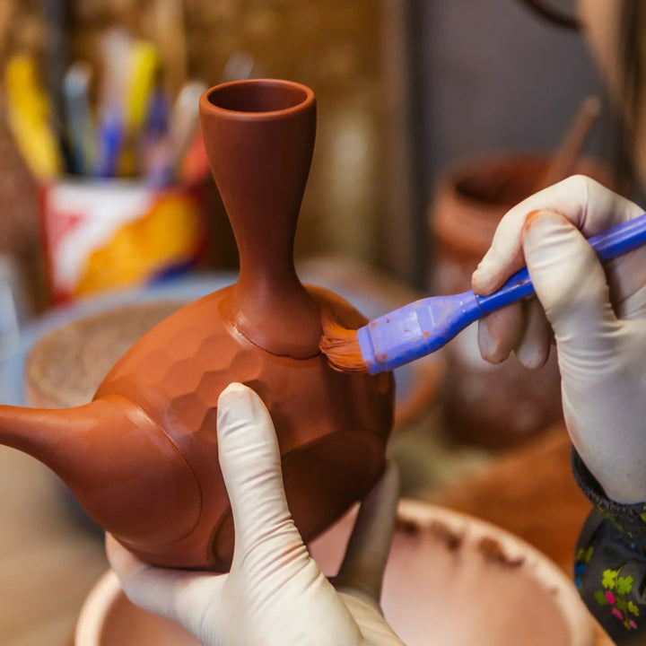Artisan brushing a clay teapot with precise hand finishing to enhance its surface texture in a pottery studio
