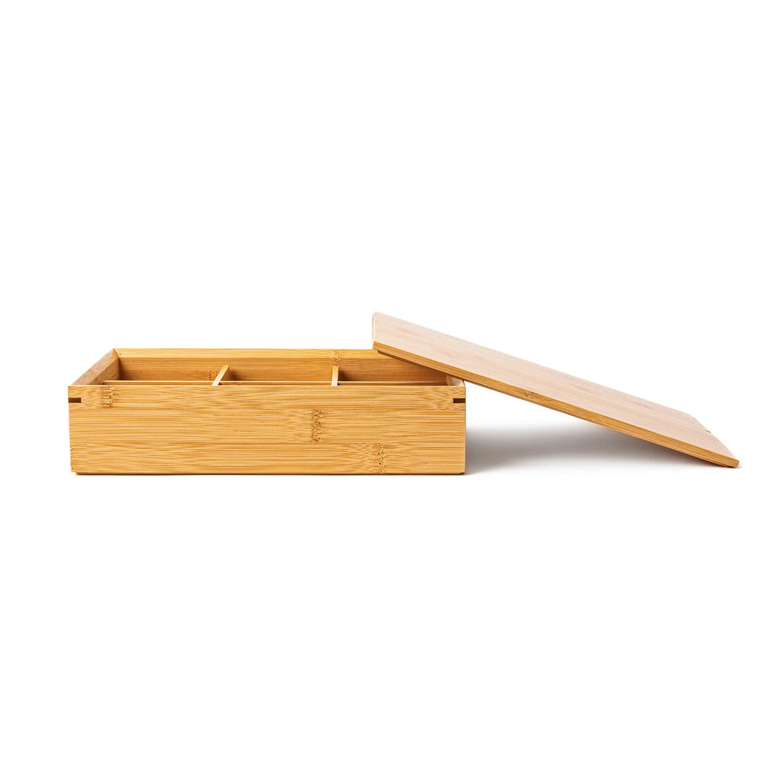 An open six compartment bamboo bento box viewed from the side with its flat lid leaning on the edge showing a sleek profile