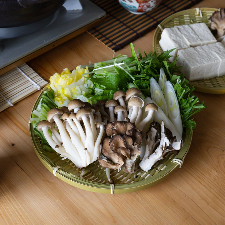 Traditional Japanese bamboo zaru strainer basket filled with fresh shimeji mushrooms and vegetables for hot pot dinner