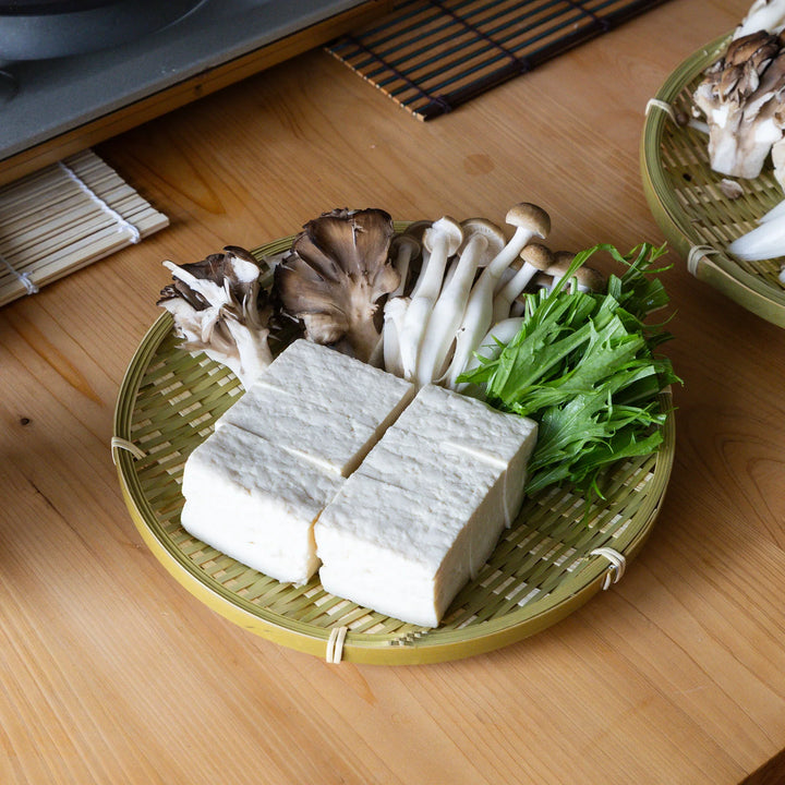 Traditional Japanese bamboo zaru strainer basket holding fresh tofu blocks and mushrooms for yudofu hot pot meal