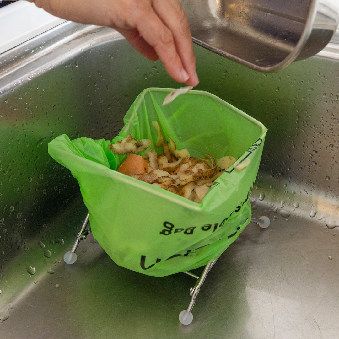 Nami throwing veggie peels into ecoframe stainless compost holder inside kitchen sink food waste bag stand