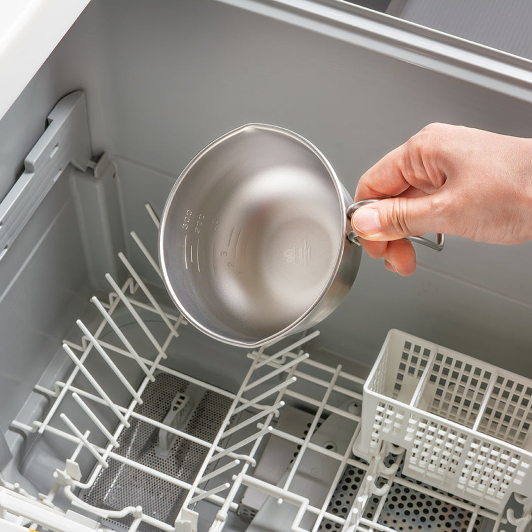 Person placing a stainless steel egg beating bowl with handle into an open dishwasher rack