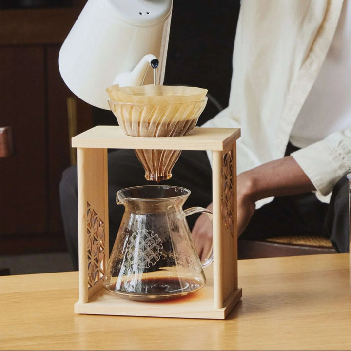 Pouring hot water from white kettle into aya asanoha wood coffee dripper set with man brewing fresh morning blend