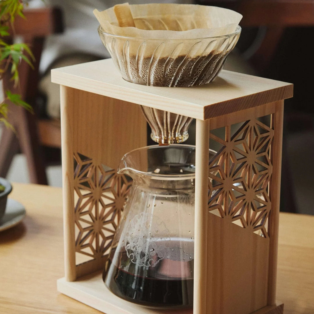 Freshly brewed coffee inside aya asanoha wood coffee dripper set sitting next to green bonsai tree on wooden table