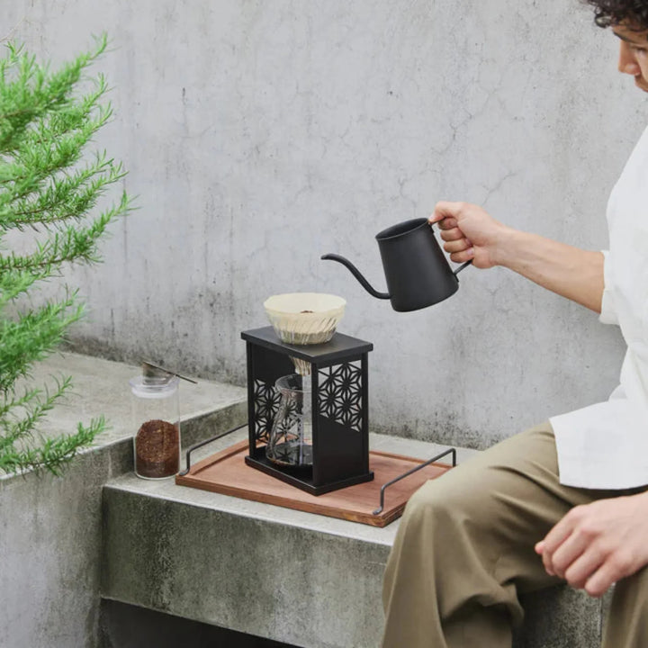 Showcasing brewed coffee inside hario aya asanoha black wood dripper set next to glass mug and small green bonsai tree