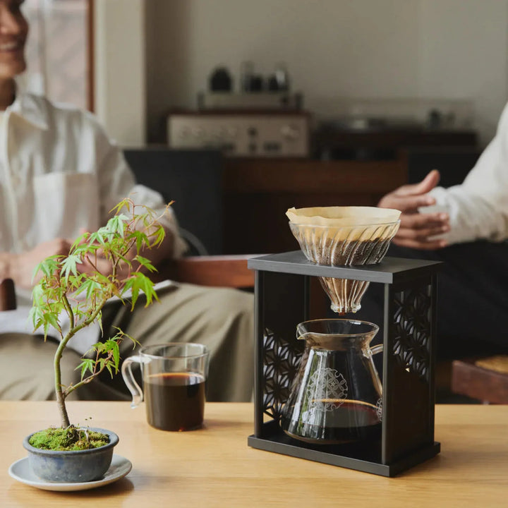 Brewing fresh pour over coffee with black hario aya asanoha wood dripper set on wooden tray in outdoor garden patio
