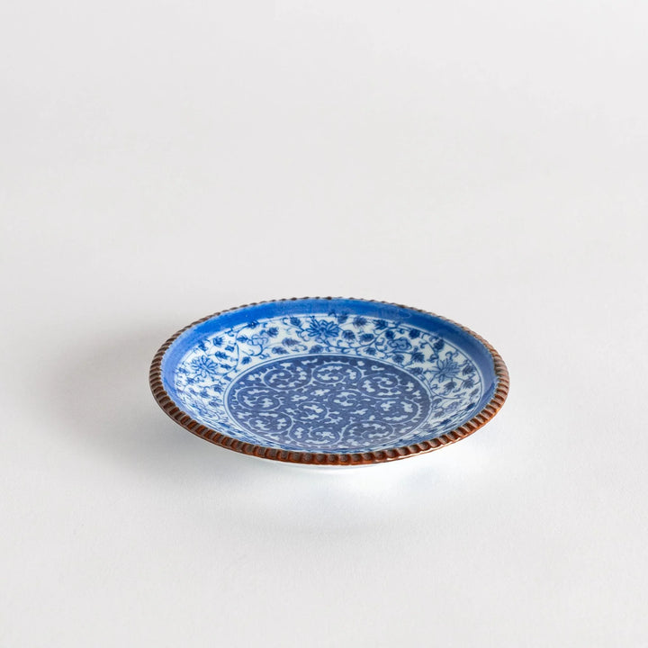 Small ceramic plate with intricate blue floral circular motif bordered by copper colored textured rim.