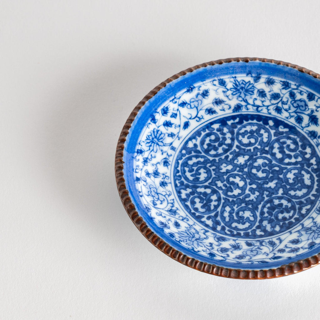 Small ceramic plate with intricate blue floral circular motif bordered by copper colored textured rim.