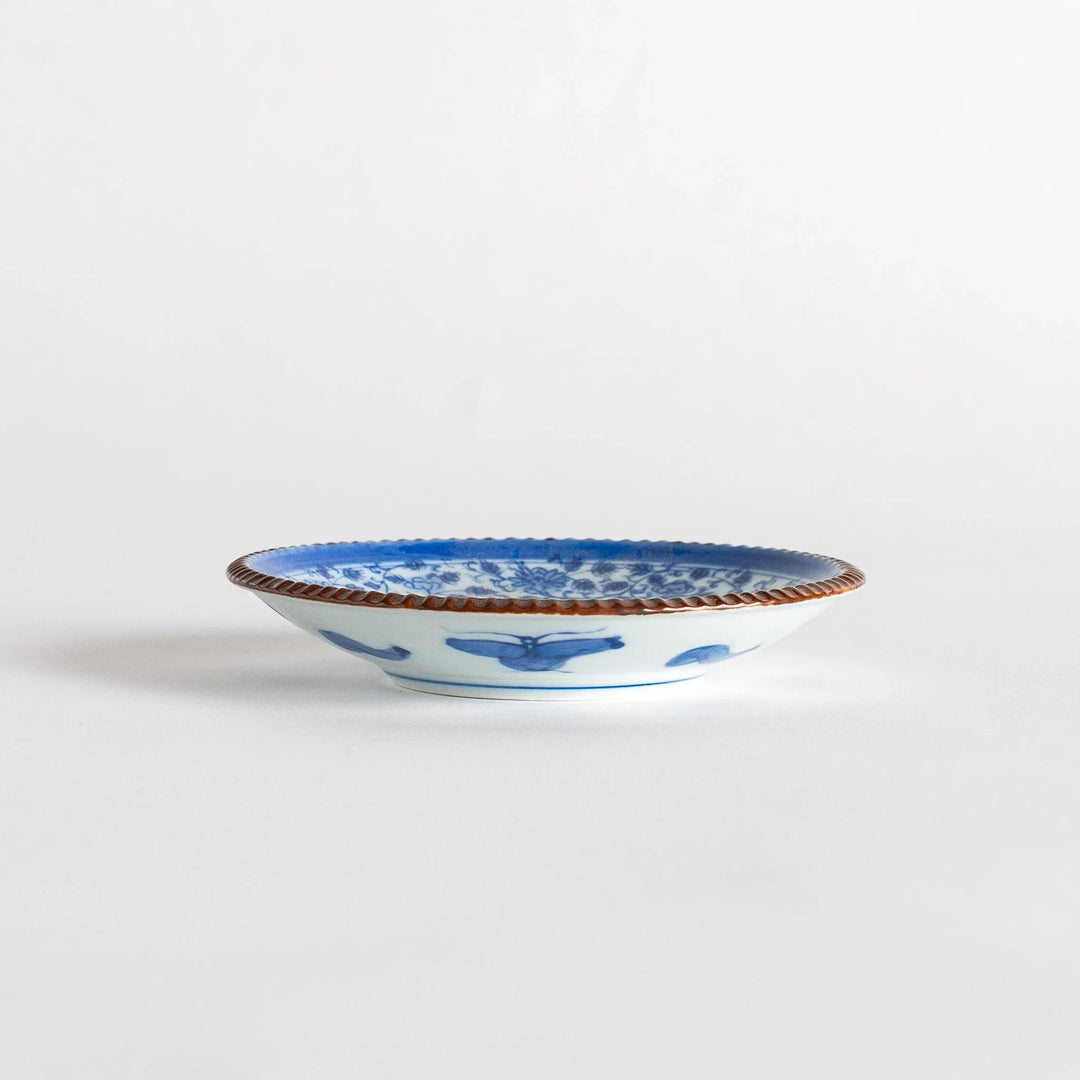 Small ceramic plate with intricate blue floral circular motif bordered by copper colored textured rim.