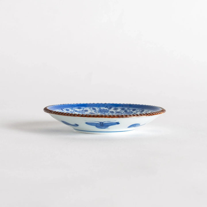 Small ceramic plate with intricate blue floral circular motif bordered by copper colored textured rim.