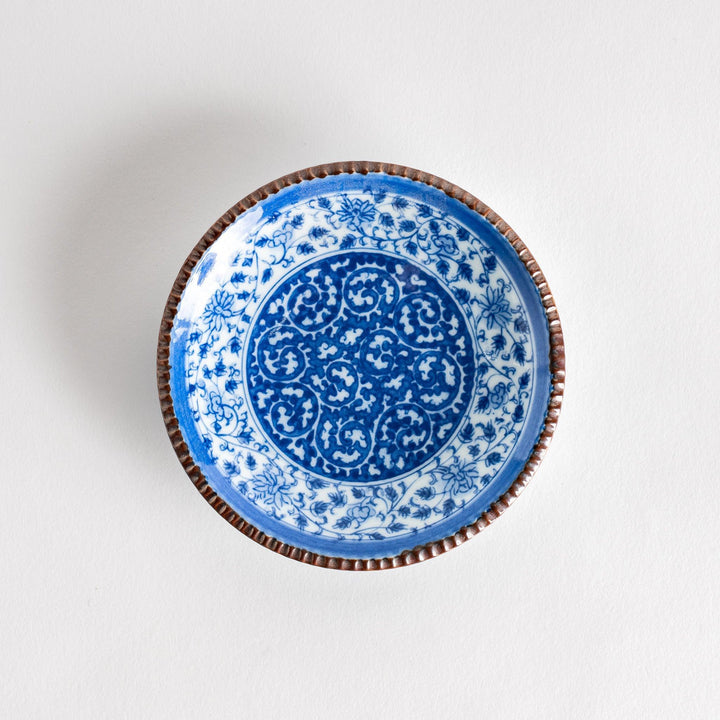 Small ceramic plate with intricate blue floral circular motif bordered by copper colored textured rim.