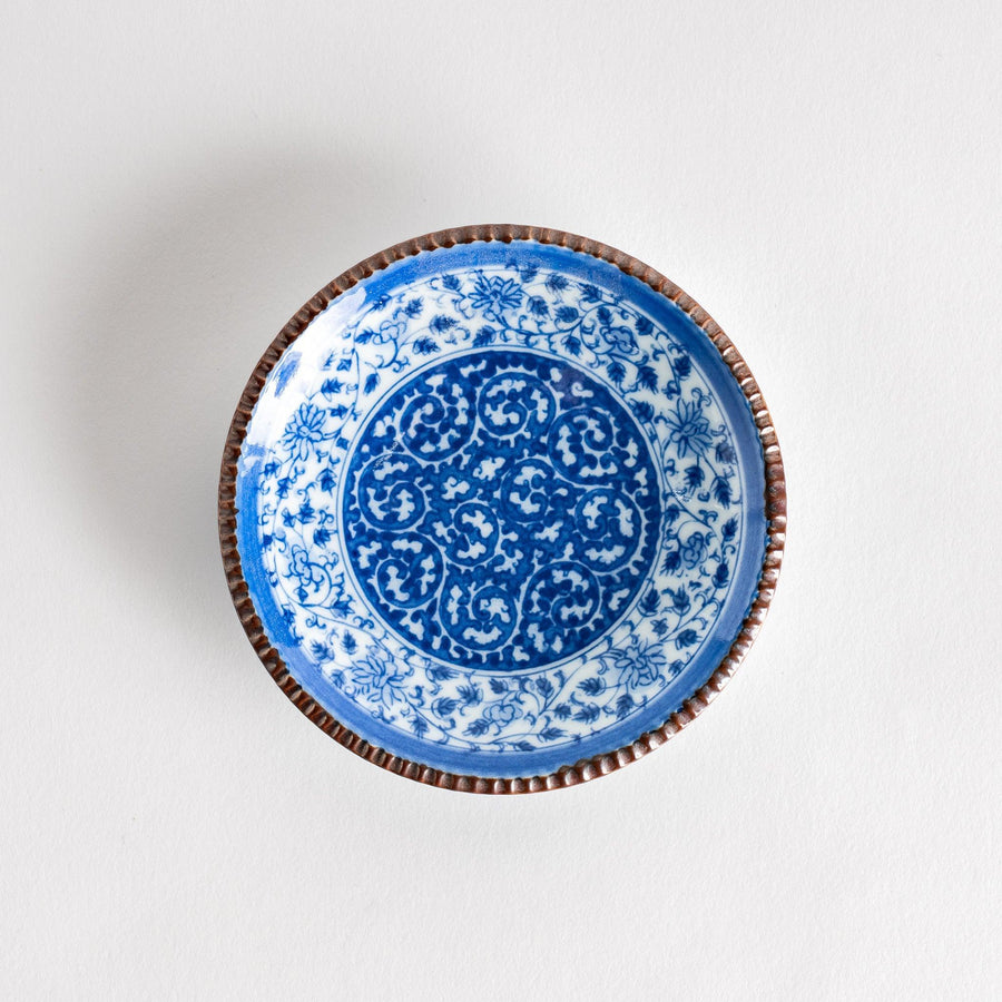 Small ceramic plate with intricate blue floral circular motif bordered by copper colored textured rim.