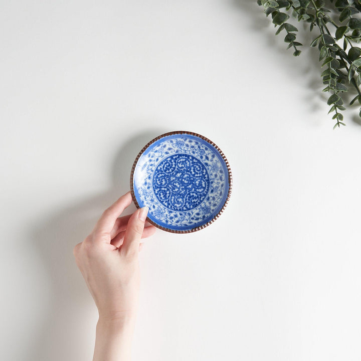 Small ceramic plate with intricate blue floral circular motif bordered by copper colored textured rim.