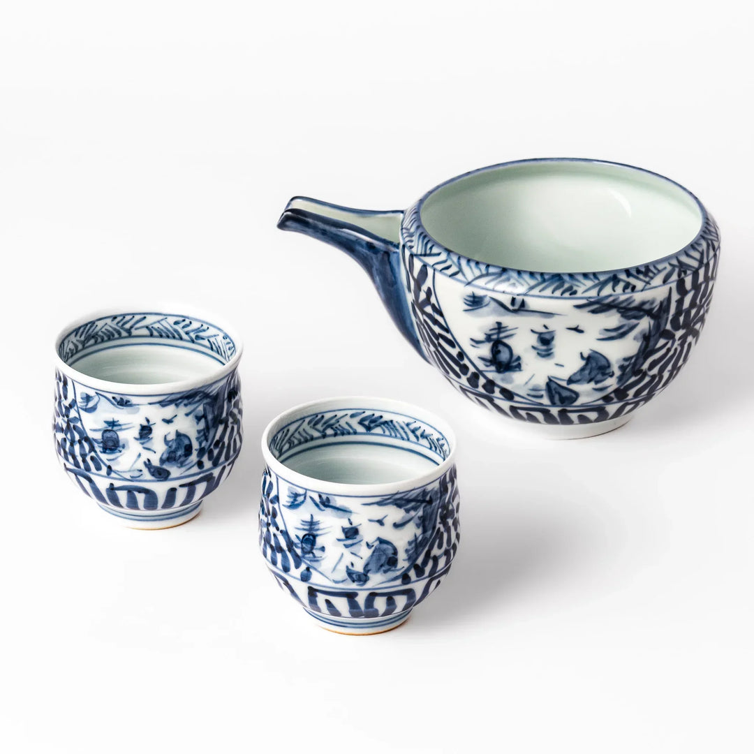 Porcelain sake set with a spouted pourer and two cups decorated with hand painted indigo landscape and arabesque motifs.