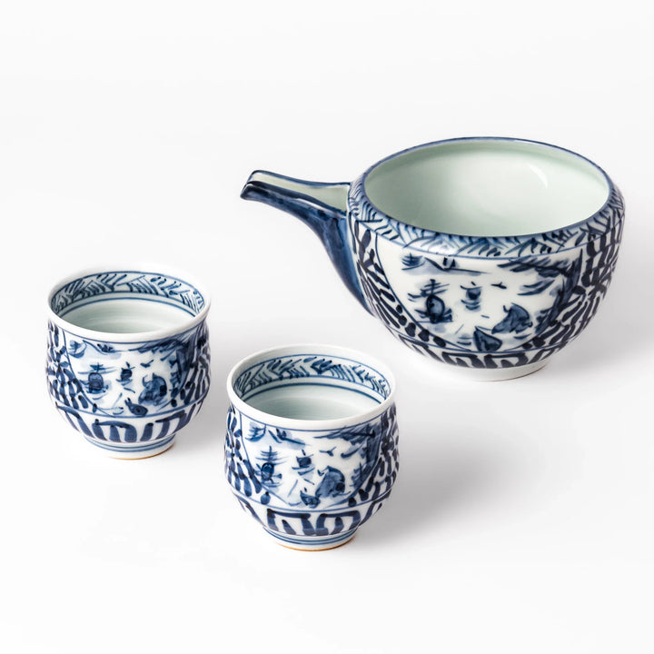 Porcelain sake set with a spouted pourer and two cups decorated with hand painted indigo landscape and arabesque motifs.