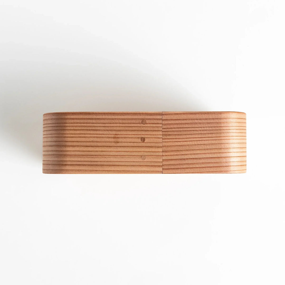 Side view of the Artisan Cedar Bento Box, showcasing its sleek, striped texture and smooth, rounded edges with visible joinery details.