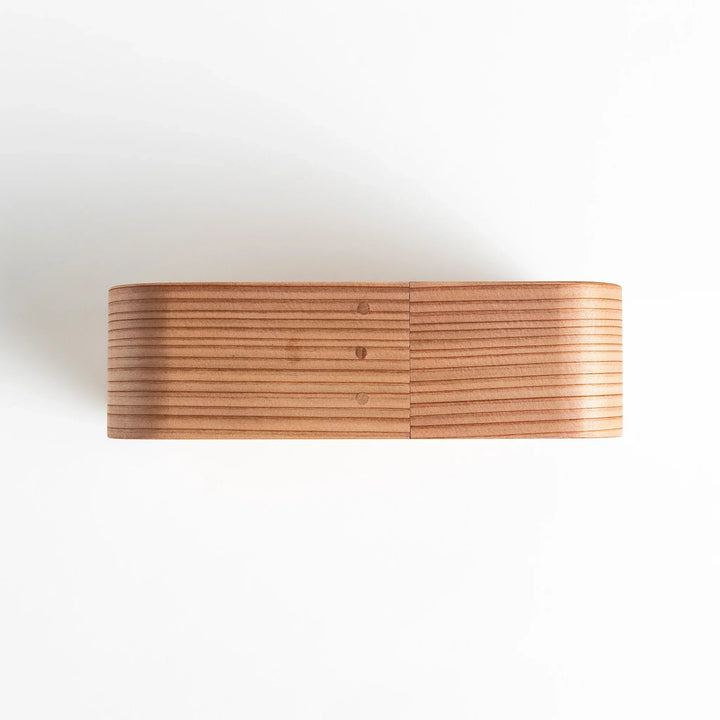 Side view of the Artisan Cedar Bento Box, showcasing its sleek, striped texture and smooth, rounded edges with visible joinery details.