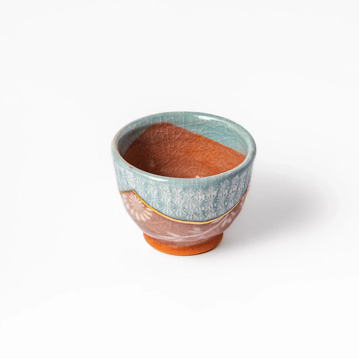 Turquoise crackle-glazed ceramic tea cup with floral patterns and earthy brown base, highlighting handcrafted beauty.