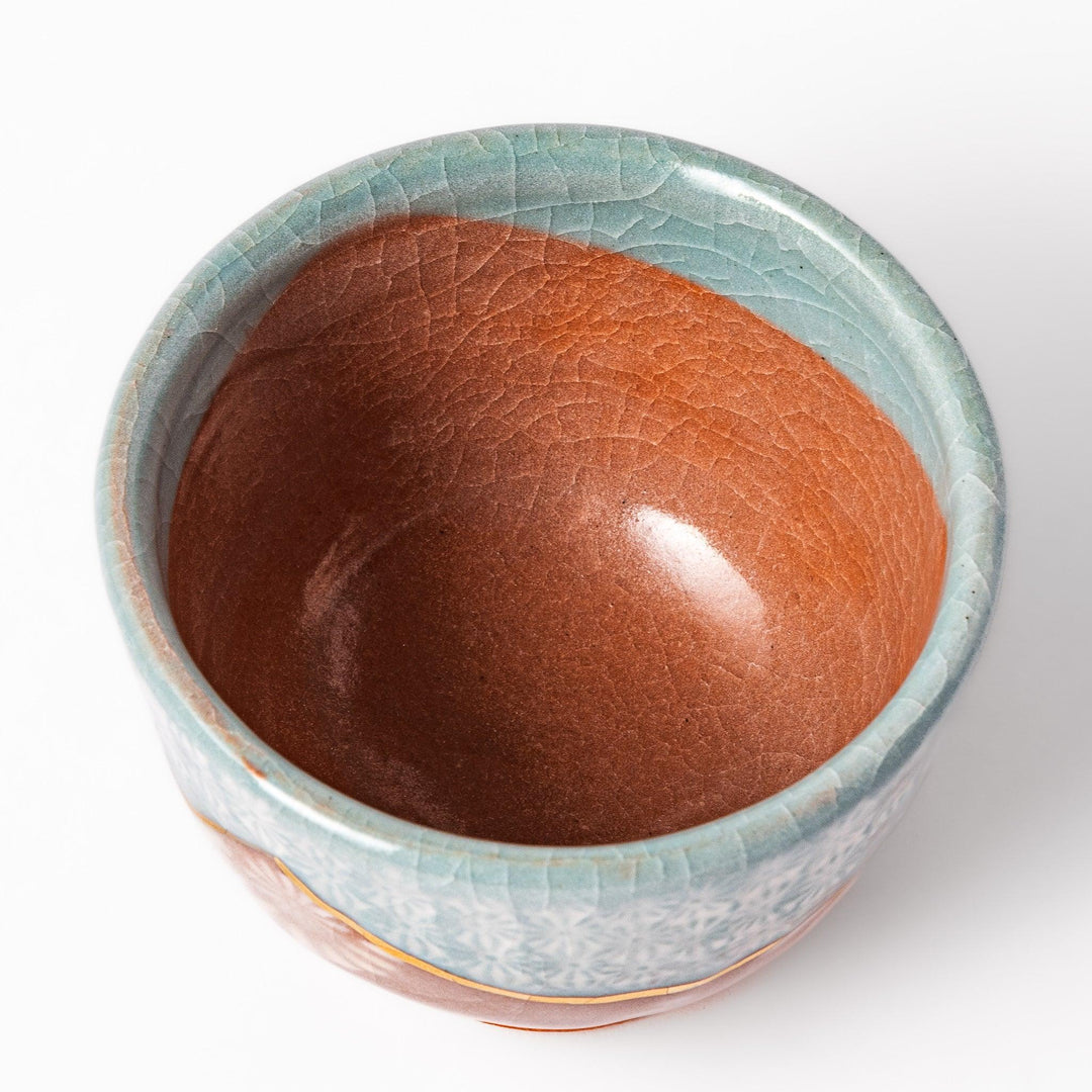 Turquoise crackle-glazed ceramic tea cup with floral patterns and earthy brown base, highlighting handcrafted beauty.
