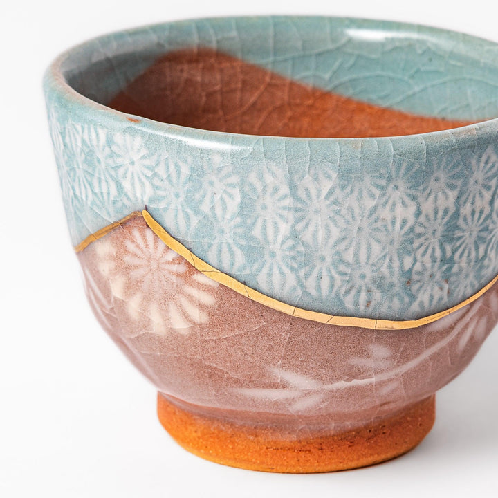 Turquoise crackle-glazed ceramic tea cup with floral patterns and earthy brown base, highlighting handcrafted beauty.