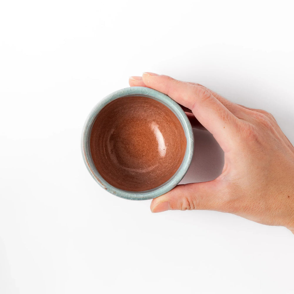 Turquoise crackle-glazed ceramic tea cup with floral patterns and earthy brown base, highlighting handcrafted beauty.