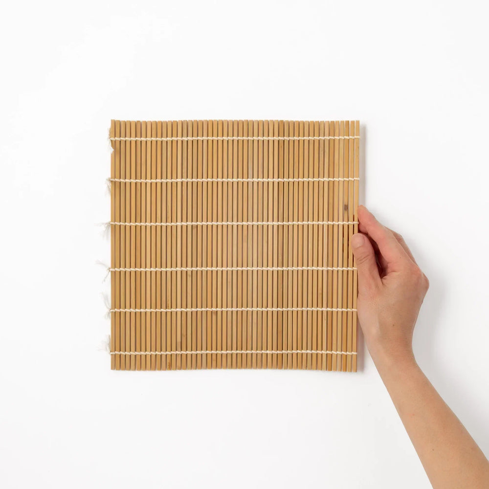 Traditional bamboo sushi rolling mat with uniform slats and white cotton string for home sushi making.