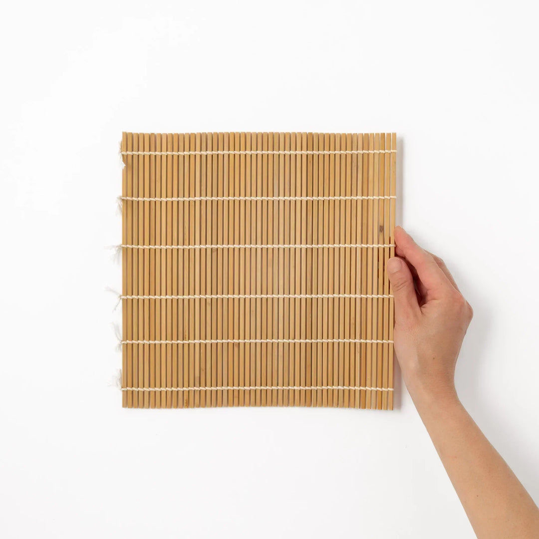 Traditional bamboo sushi rolling mat with uniform slats and white cotton string for home sushi making.