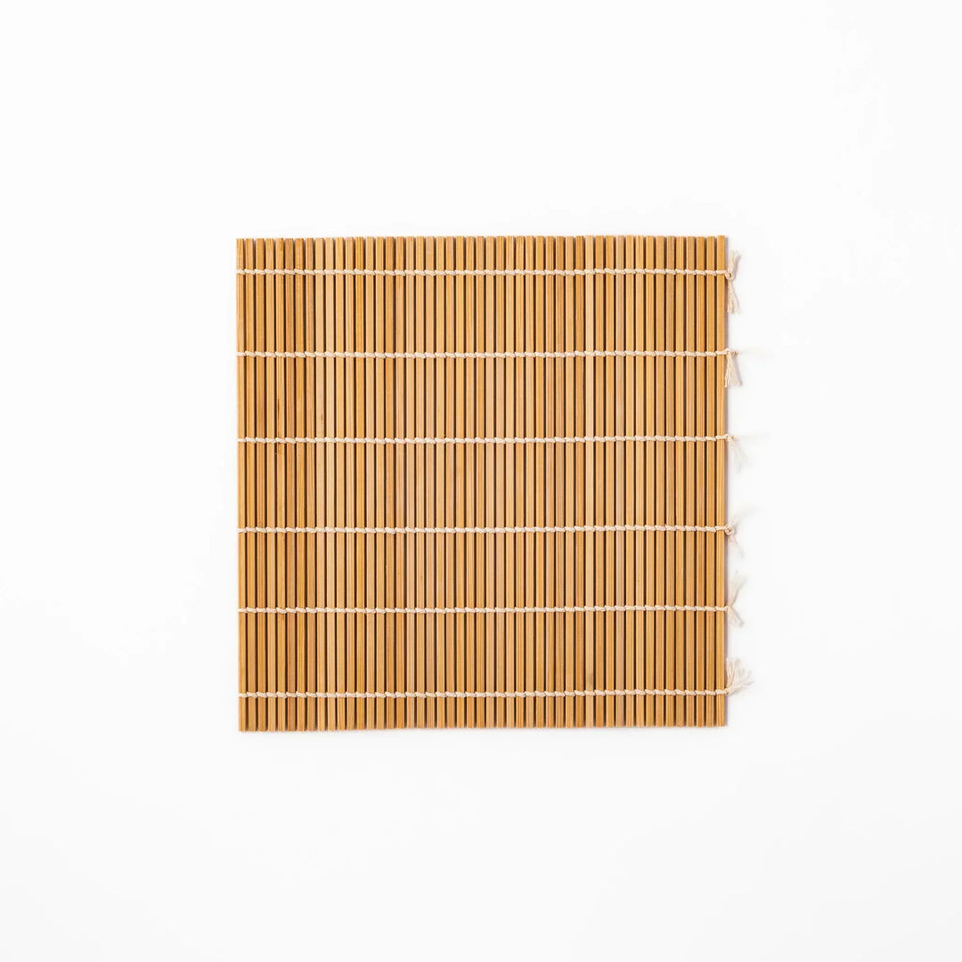 Traditional bamboo sushi rolling mat with uniform slats and white cotton string, partially rolled to show flexibility for making perfect sushi at home.