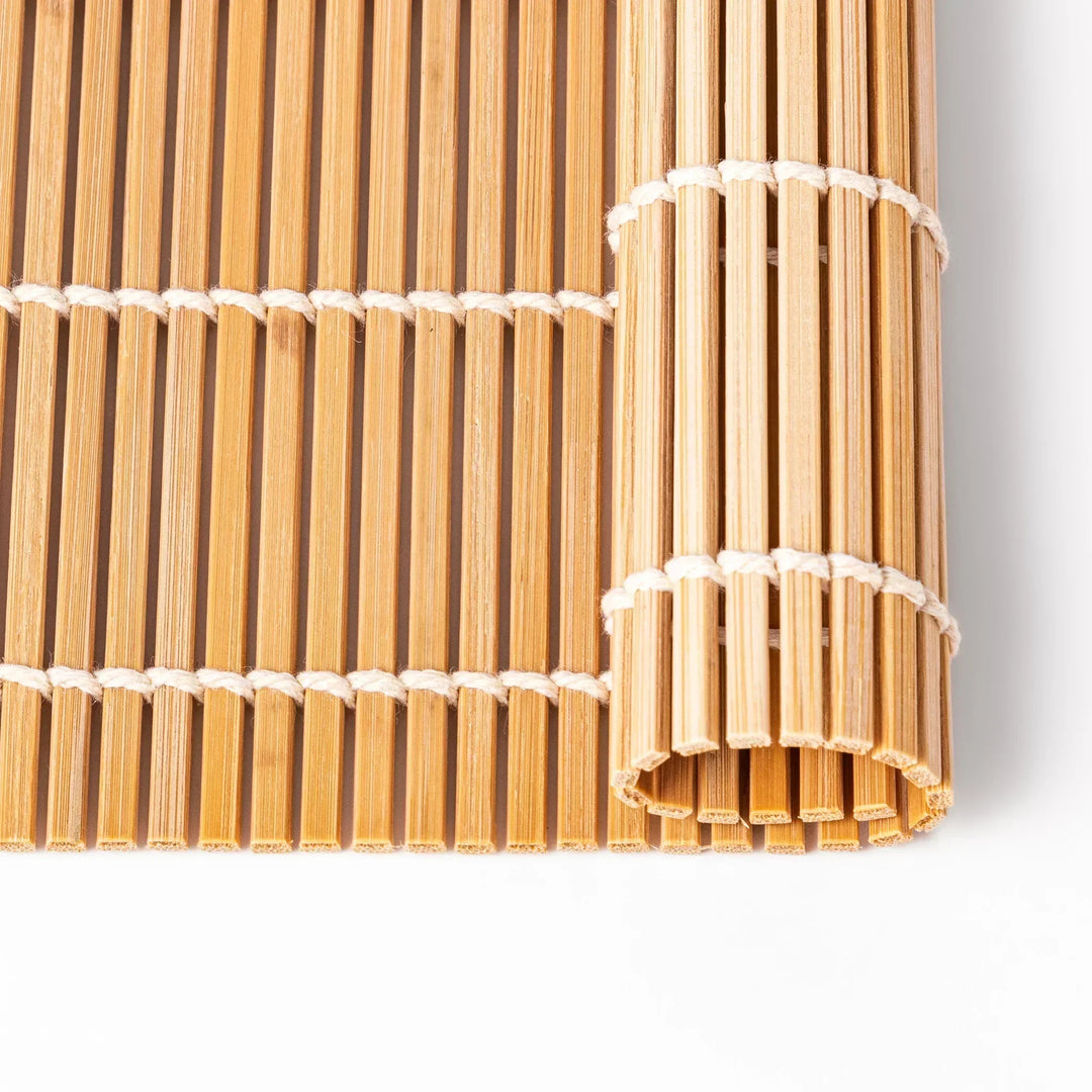 Traditional bamboo sushi rolling mat with uniform slats and white cotton string for home sushi making.