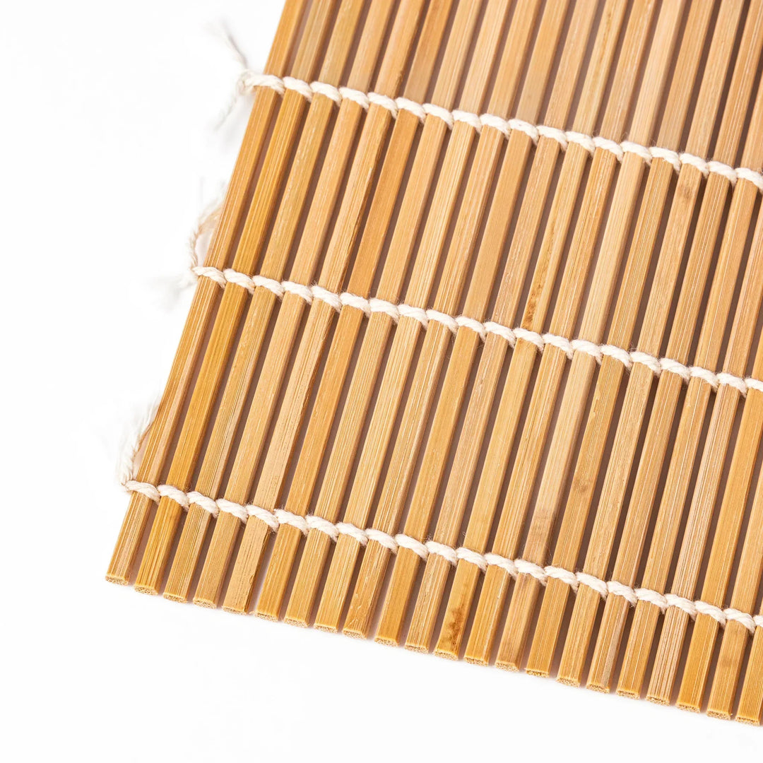 Traditional bamboo sushi rolling mat with uniform slats and white cotton string for home sushi making.