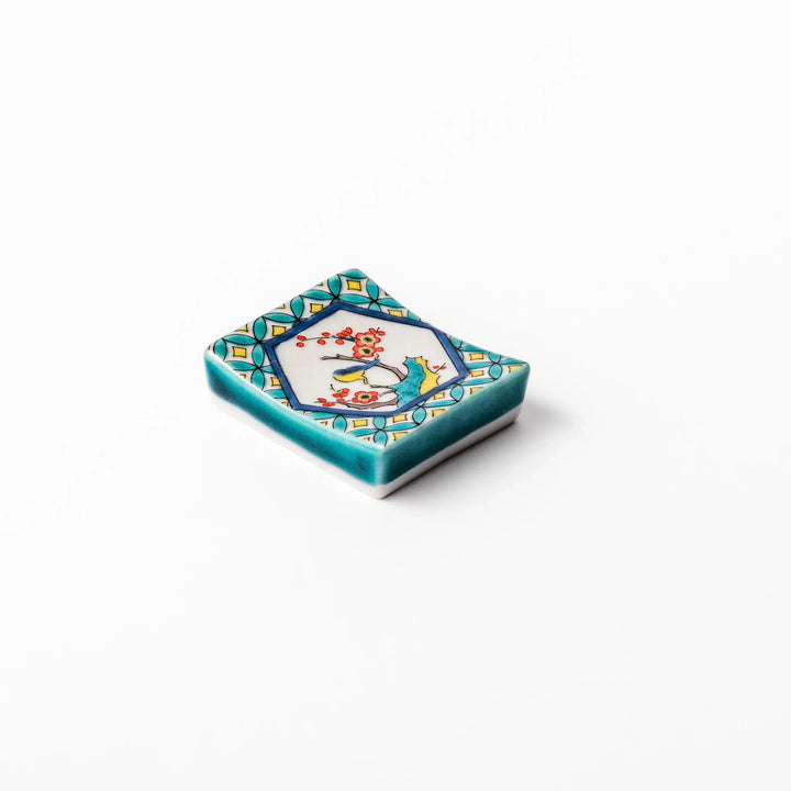 Rectangular Japanese ceramic chopstick rest with turquoise border and central motif of bird on plum blossoms in vivid colors.