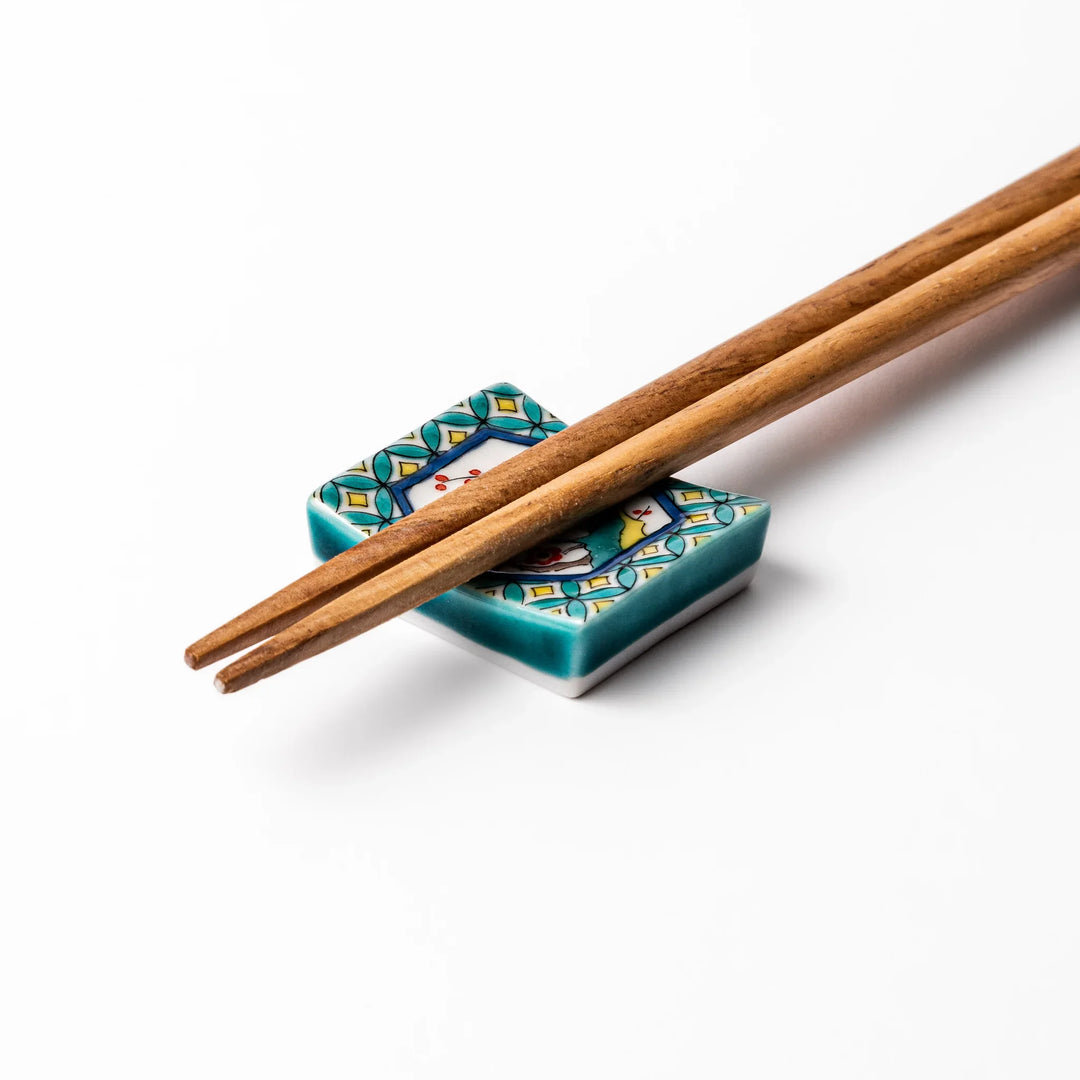 Rectangular Japanese ceramic chopstick rest with turquoise border and central motif of bird on plum blossoms in vivid colors.