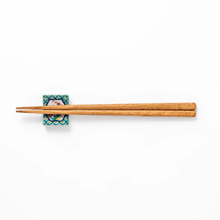 Rectangular Japanese ceramic chopstick rest with turquoise border and central motif of bird on plum blossoms in vivid colors.