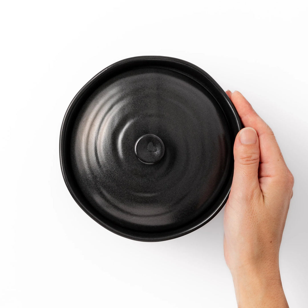 Black ceramic rice storage bowl with floral ridge lid design, compact size for storing cooked rice and keeping it warm.